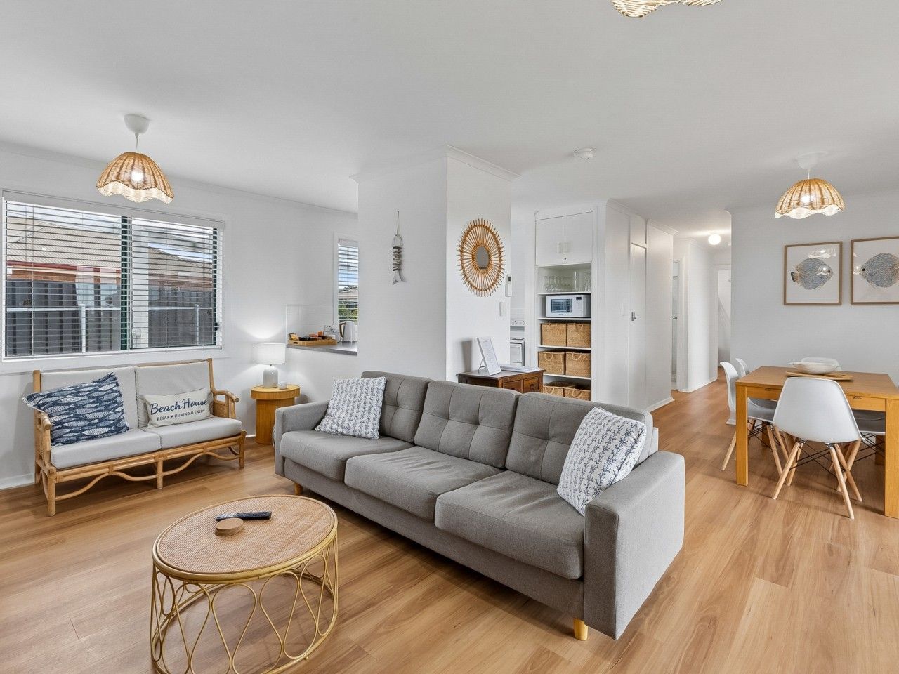 A modern living room with a grey sofa, a round wicker coffee table, and a dining area with a wooden table and chairs.