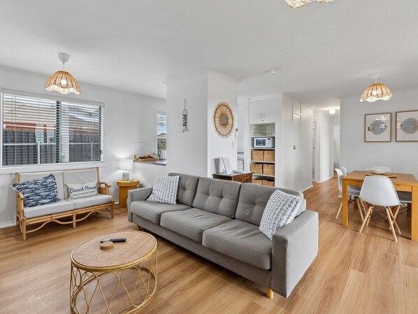 A modern living room with a grey sofa, a round wicker coffee table, and a dining area with a wooden table and chairs. - Coastal Break - Family Escape in Port Hughes (Port Hughes)