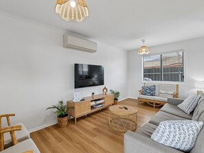 A modern living room with a flat-screen TV, a sofa, a coffee table, and a wicker side table. - Coastal Break - Family Escape in Port Hughes (Port Hughes)