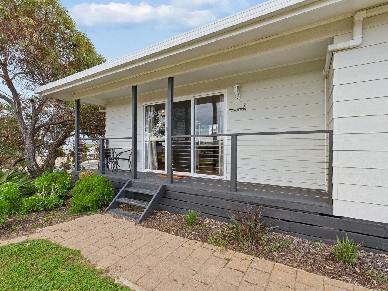A single-story building with a covered porch, a set of stairs leading to the entrance, and a small garden area with shrubs and a paved walkway.