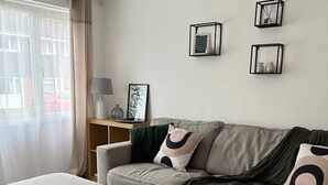 Ett modernt vardagsrum med en grå soffa, en tillhörande pall och ett sidobord med en lampa och fotobilder.