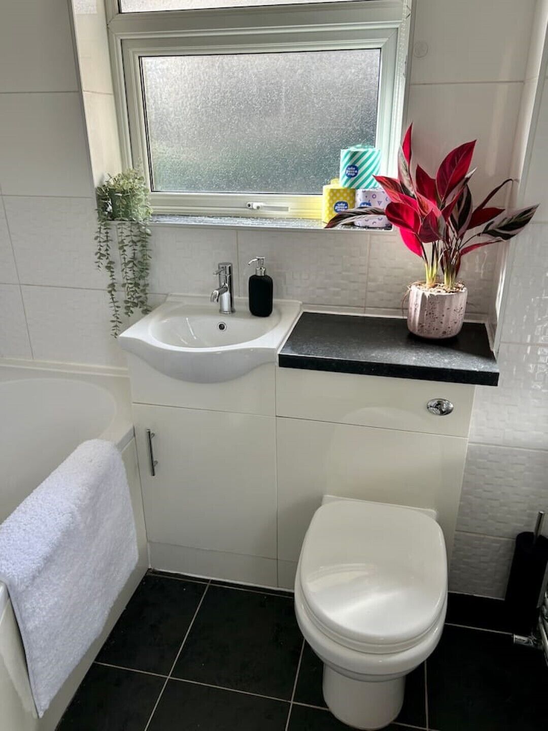 A bathroom with a white sink, a toilet, and a window above the sink.