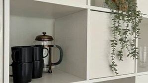 Ett vitt skåp med en fransk presskanna, svarta muggar och en vit vas.