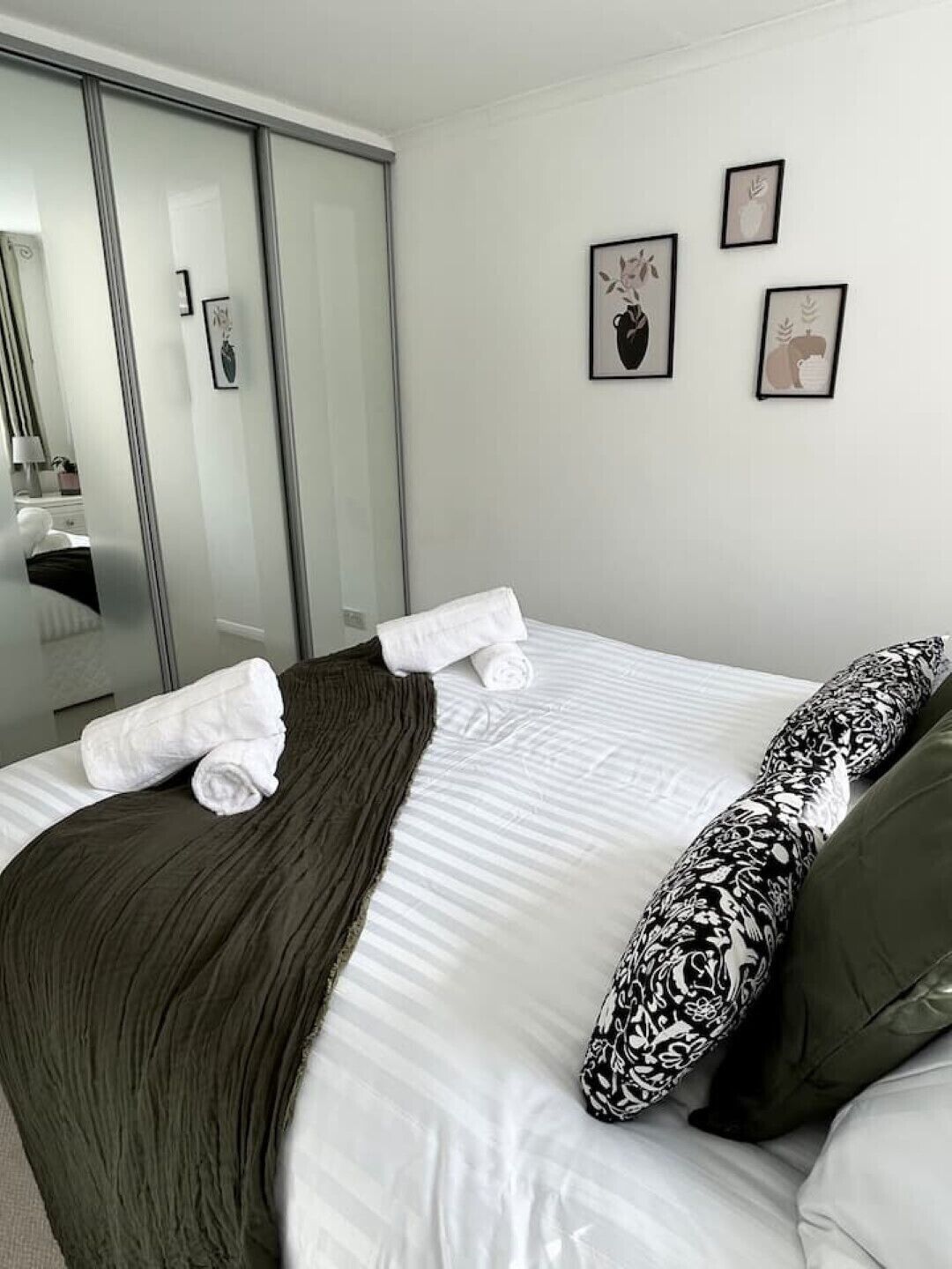 Ein Hotelzimmer mit einem Bett, einem großen Spiegel und drei gerahmten Bildern an der Wand.
