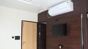 A room with a wooden door, a mounted air conditioner, a flat-screen TV, and a wall-mounted light switch. - FERN INN Kolkata (Kolkata)