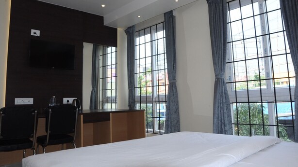 A hotel room with a large bed, two chairs, a desk, and a TV mounted on the wall. - FERN INN Kolkata (Kolkata)