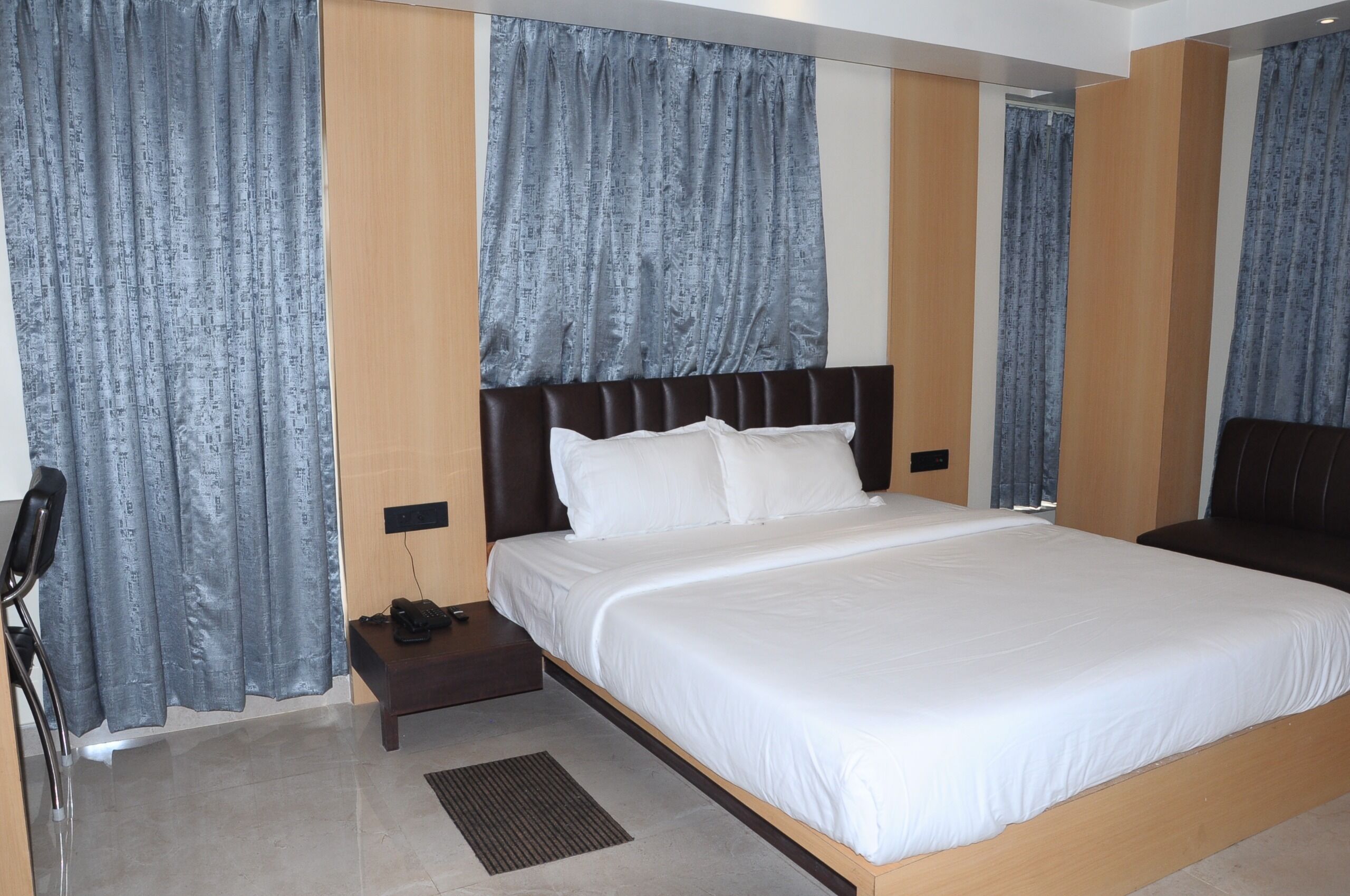 Una habitación de hotel con una cama grande, una mesita de noche con un teléfono y cortinas en las ventanas.
