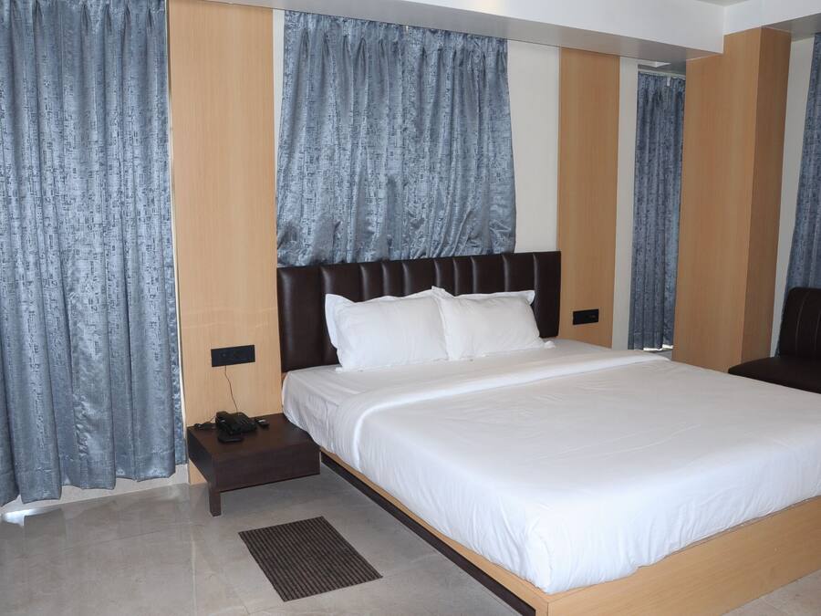 A hotel room with a large bed, a bedside table with a phone, and curtains on the windows.