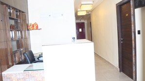 A reception area with a reception desk, a wooden cabinet, and a door in the background. - FERN INN Kolkata (Kolkata)