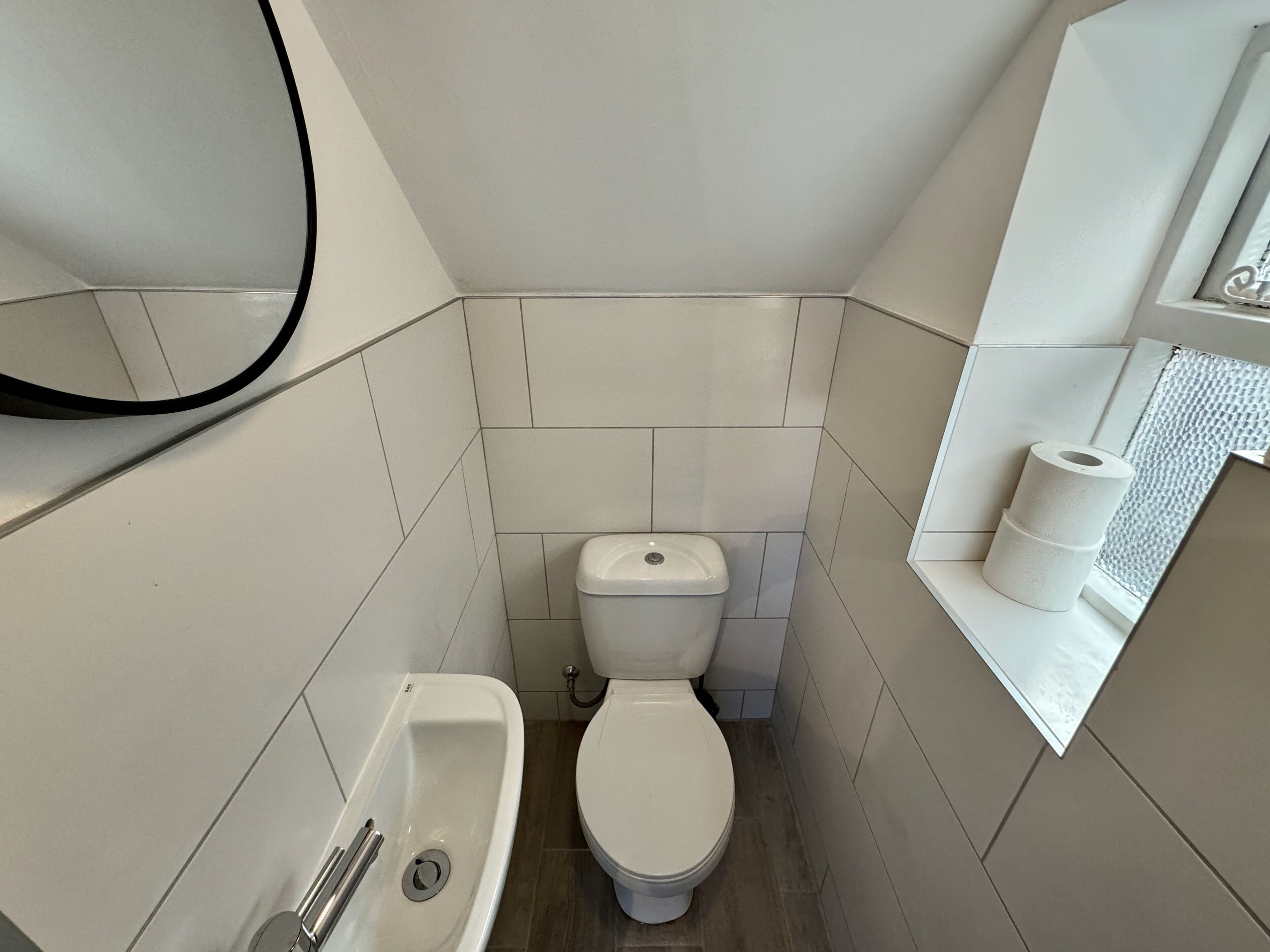 A small, modern bathroom with a toilet, a sink, and a mirror.