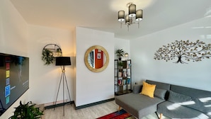 A modern living room with a grey sofa, a colorful striped rug, a round mirror, a bookshelf, and a TV on the left. - Sandringham House Serene Escape Cottage (Cleethorpes)