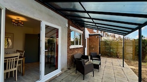 A covered patio with outdoor furniture, a sliding glass door leading to an interior room, and a brick wall. - Sandringham House Serene Escape Cottage (Cleethorpes)