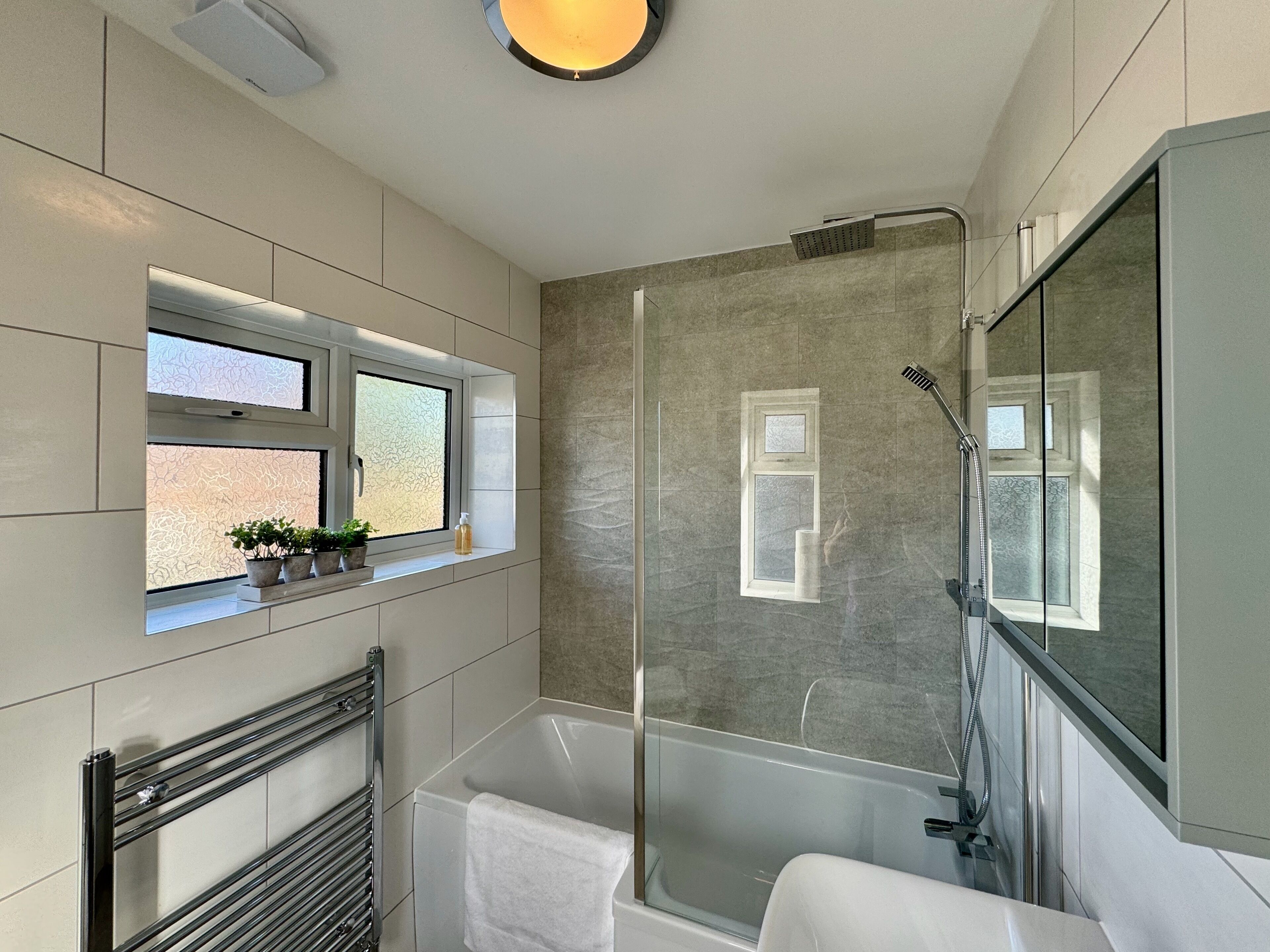 A modern bathroom with a glass-enclosed shower, a built-in window with plants, and a large mirror.