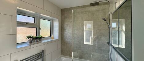 A modern bathroom with a glass-enclosed shower, a built-in window with plants, and a large mirror.