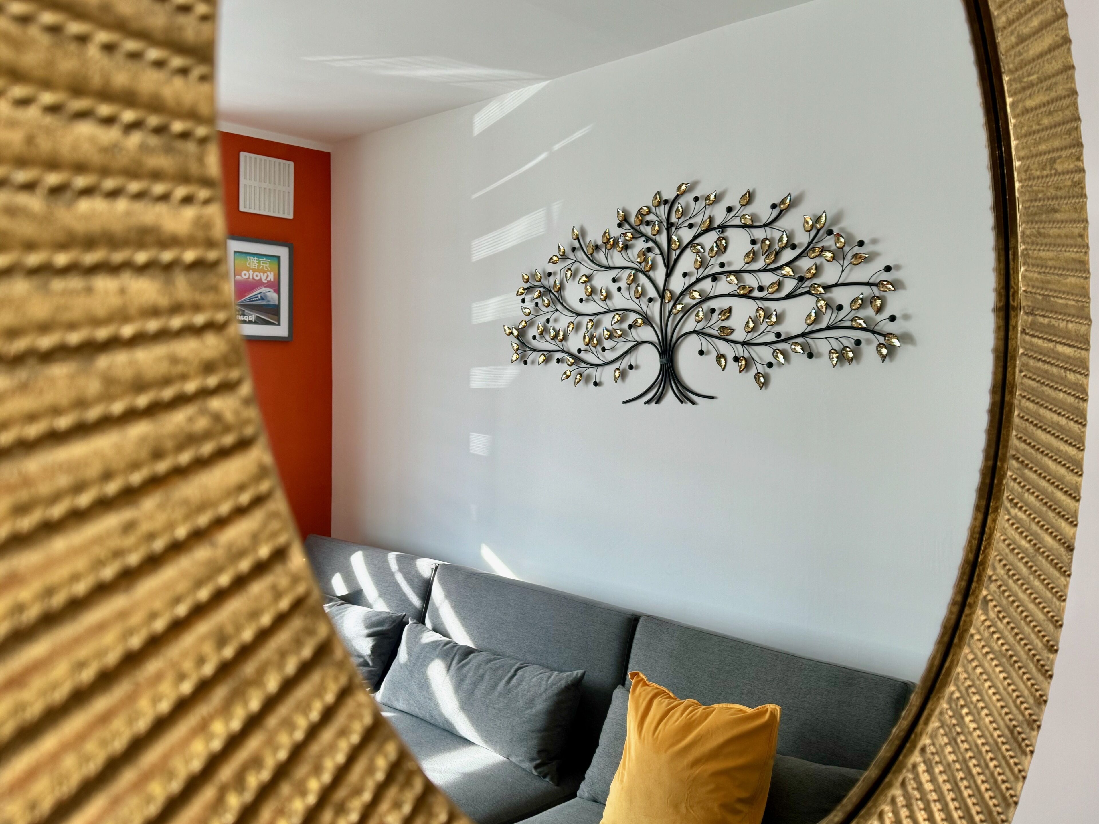 A modern living room with a gray sofa, a yellow pillow, and a wall-mounted tree decoration.