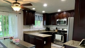 Une cuisine moderne avec des meubles en bois foncé, un comptoir en granit, un îlot central intégré, une table à manger avec des chaises et un ventilateur de plafond.