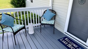 Une véranda avec deux fauteuils en osier, un panier blanc et un paillasson.