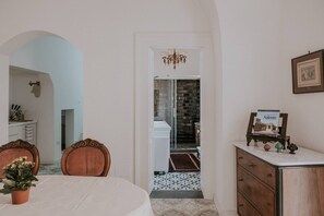A dining area with a table and chairs, a chandelier, a dresser with a picture frame, and a doorway leading to a bathroom with a tiled floor.