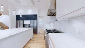 Una cocina moderna con armarios blancos, una isla central, electrodomésticos de acero inoxidable y piso de madera.
