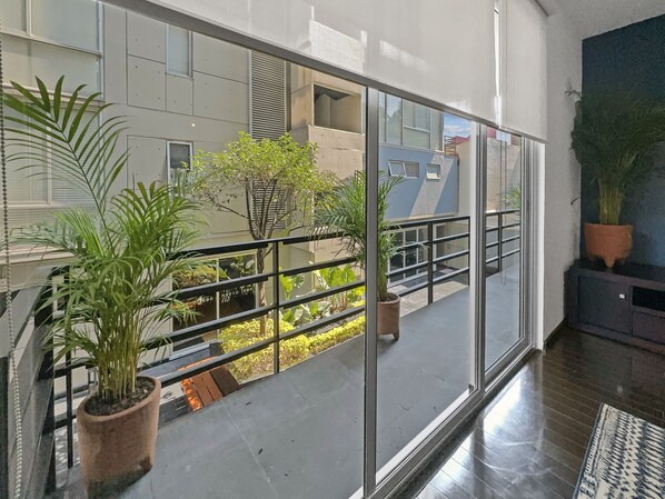 A modern interior with a glass balcony, potted plants, and a view of the outside building.