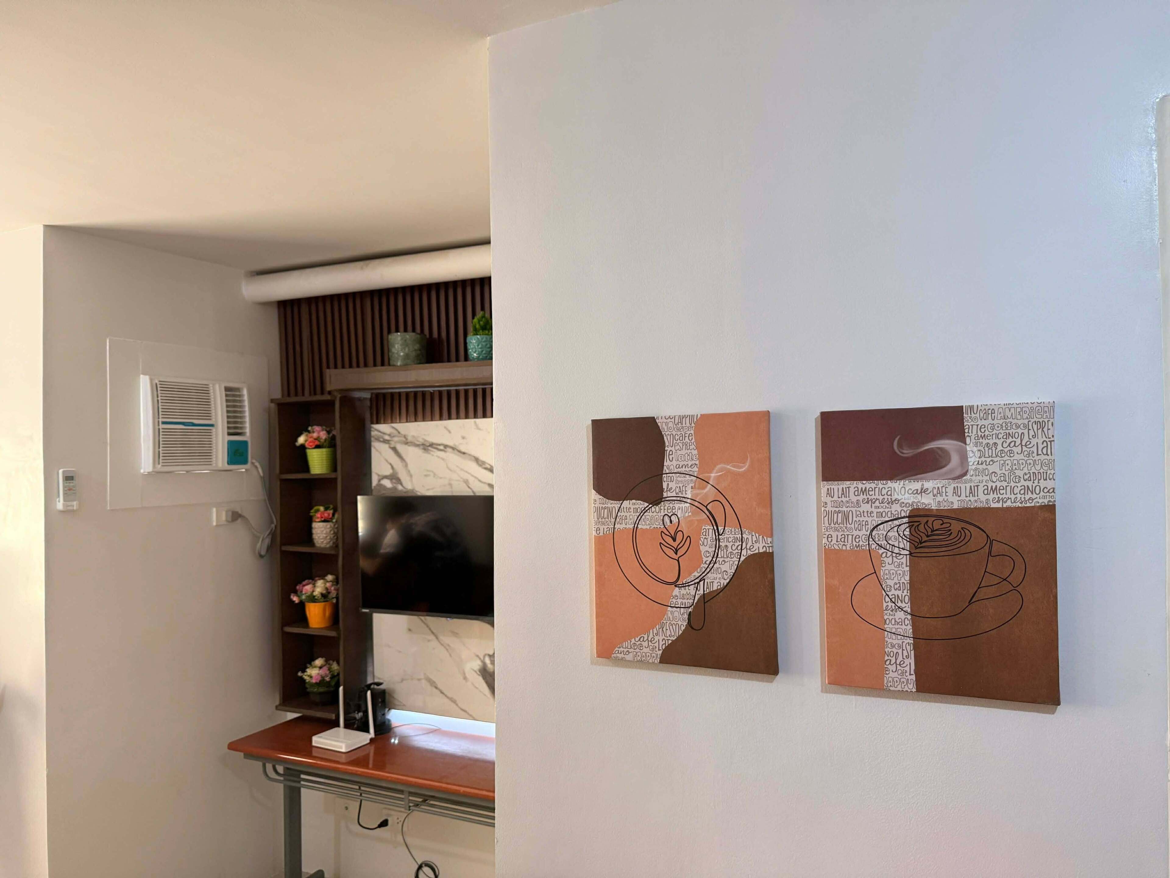 A room with a TV, a shelf with decorative items, and two abstract wall art pieces.