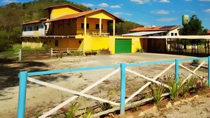 A yellow building with a green garage door, a fenced area with plants, and a clear sky. - Pousada Sunflower (Pirenópolis)