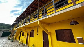 A yellow building with a balcony, wooden doors, and a stone floor. - Pousada Sunflower (Pirenópolis)