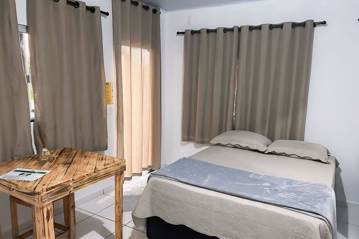 A bedroom with a bed, curtains, a wooden table, and a window.