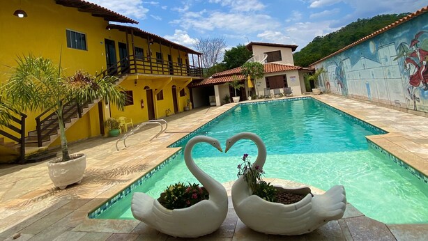 A swimming pool with two swan-shaped planters, a yellow building, and a mural on the wall. - Pousada Sunflower (Pirenópolis)