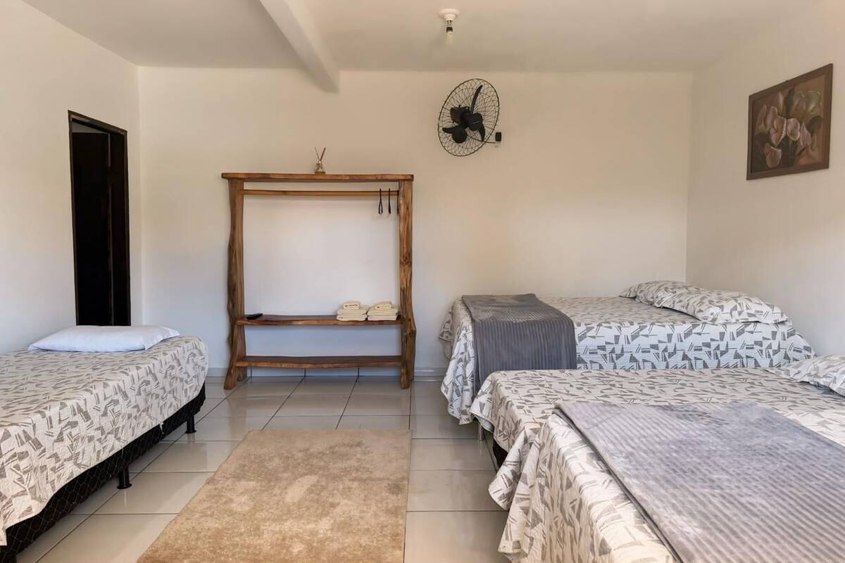 A bedroom with three beds, a wooden bench, a fan, and a door.