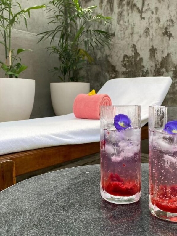 Two glasses of red beverage with ice and a flower on a table, a white lounge chair, and two potted plants in the background. - Baron's Villa by Malabar Escapes (Kochi)
