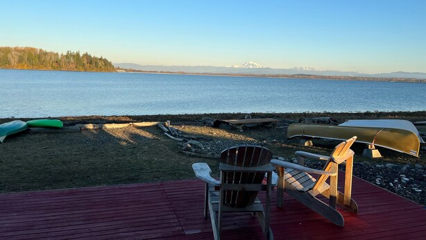 A wooden deck with a chair and a canoe, overlooking a calm lake with mountains in the distance. - Sandy Point Shalom - Ocean access and sunrise view - 20 mins to Bellingham (Ferndale)