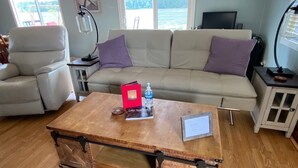 A living room with a wooden coffee table, a sofa, and a chair. There is a lamp, a TV, and a cabinet with a glass door. - Sandy Point Shalom - Ocean access and sunrise view - 20 mins to Bellingham (Ferndale)