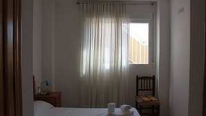 A hotel room with a bed, a chair, a desk with a lamp, and a window with curtains.
