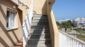 A set of stone stairs leading to a balcony with a white railing, overlooking a residential area with buildings and trees.