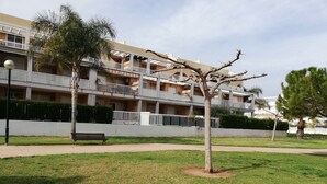 A multi-story residential building with balconies, a grassy lawn, and a bench.