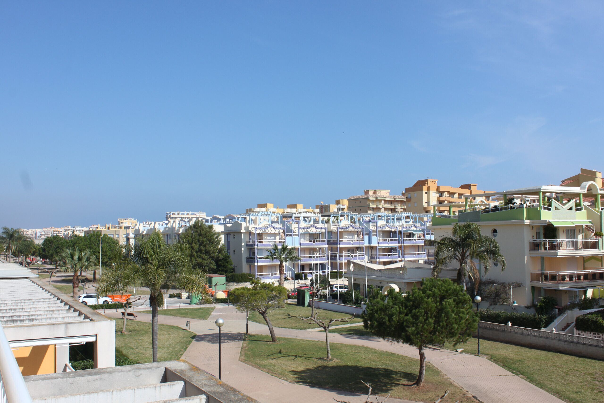 A coastal residential area with multi-story buildings, a clear sky, and a pedestrian pathway.