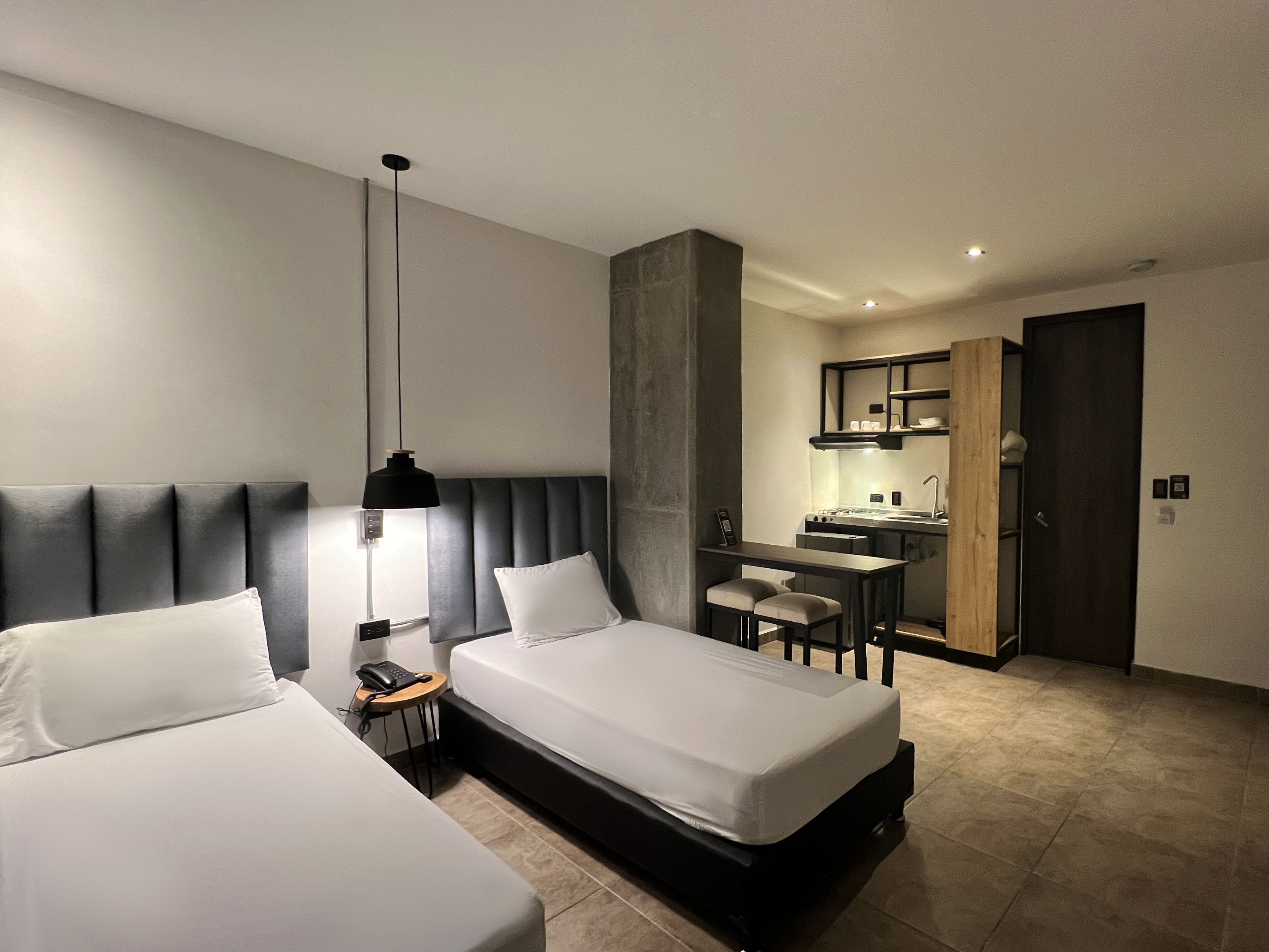 A hotel room with two beds, a desk, a chair, a phone, and a kitchenette.
