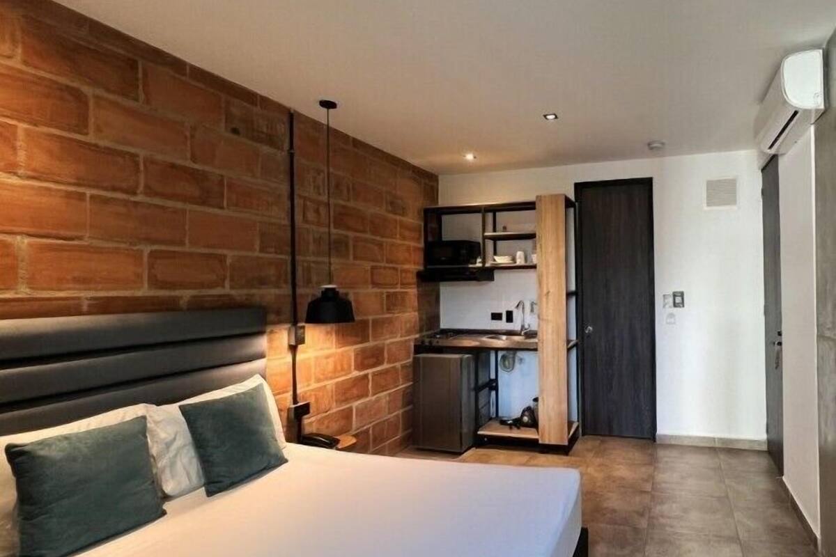 Una habitación de hotel pequeña con cama, kitchenette y pared de ladrillo.