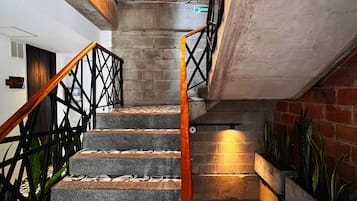 A staircase with patterned steps and a wooden handrail, leading to a landing with a metal railing and a brick wall.