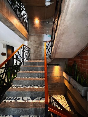 A staircase with patterned steps and a wooden handrail, leading to a landing with a metal railing and a brick wall. - Apartments Pool and Rooftop Downtown Hotel (Medellín)