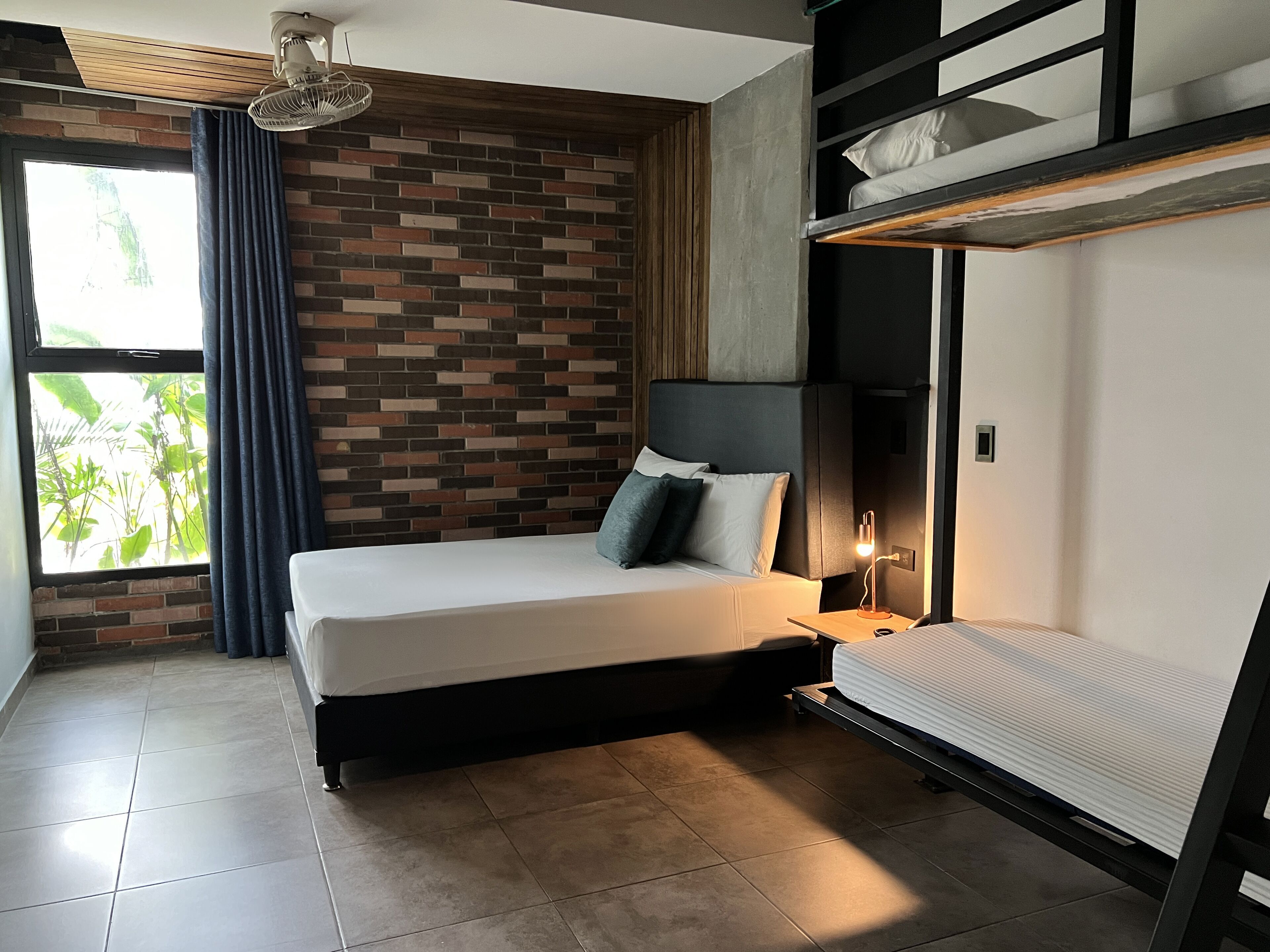 Un dormitorio moderno con pared de ladrillo, cama con cabecera, mesita de noche con lámpara y literas.