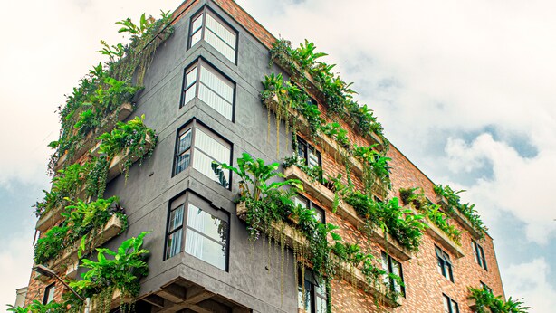 Un bâtiment moderne doté d’une architecture originale, avec de nombreux balcons ornés d’une végétation luxuriante et un logo bien visible à sa base.