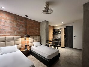 Una habitación de hotel moderna con una pared de ladrillo decorativa, una kitchenette y un área de comedor separada.