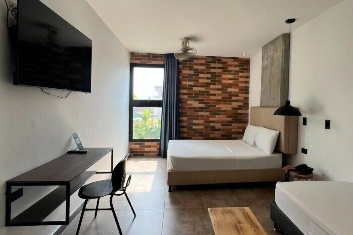 Una habitación de hotel moderna con una cama, un escritorio, una silla, un televisor y una pared con diseño de ladrillos.