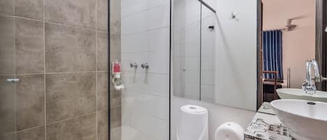 A bathroom with a glass shower enclosure, a toilet, a hand dryer, and a sink with a patterned tile backsplash.