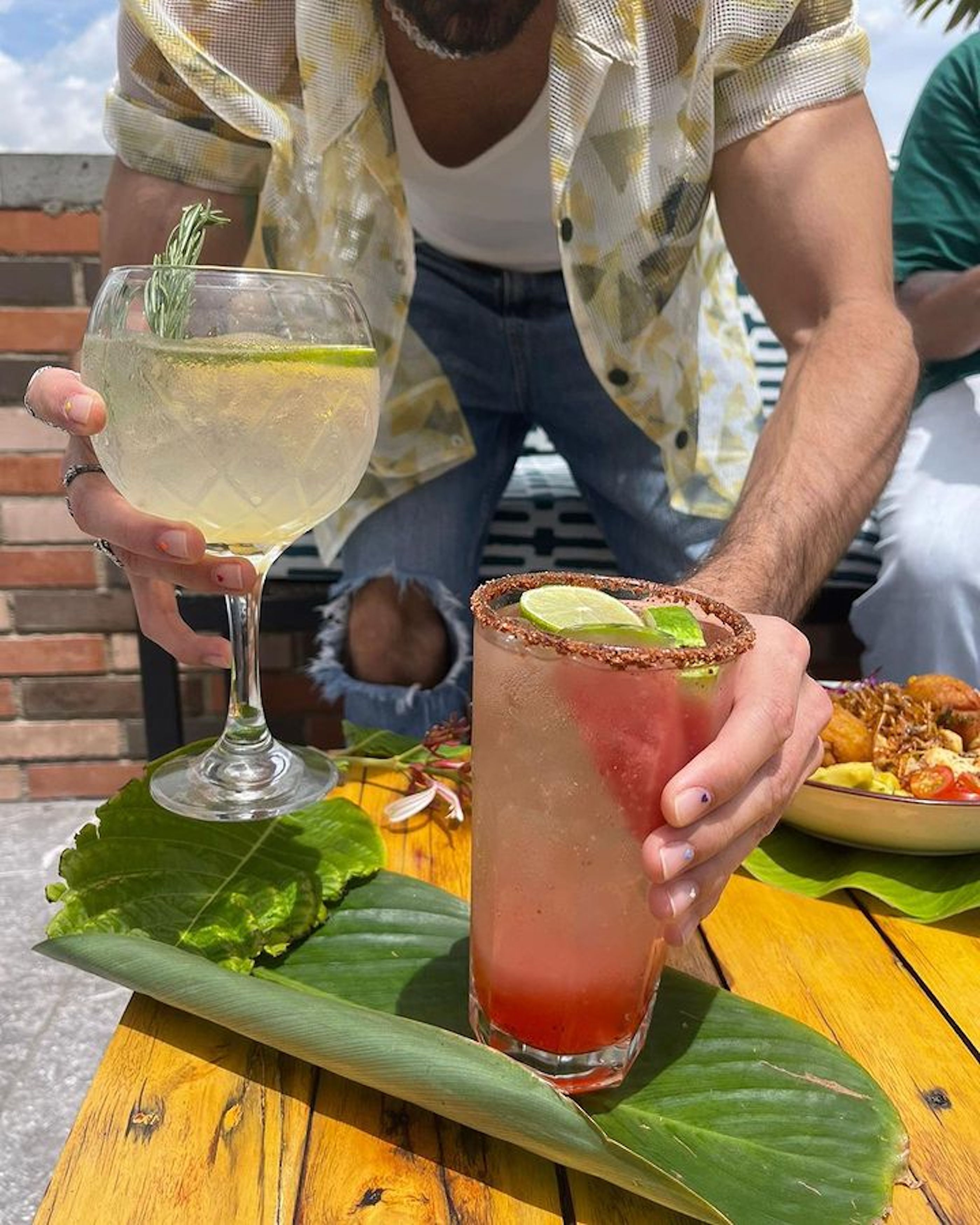 Una persona sosteniendo dos bebidas, una en un vaso y otra en un vaso alto con borde.