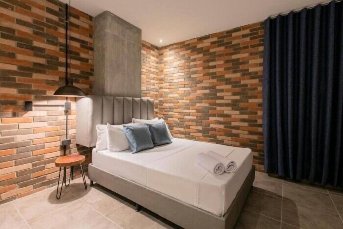 Un dormitorio moderno con una pared de ladrillo, una cama con almohadas, una mesita de noche y una lámpara.