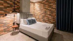 Une chambre à coucher moderne avec un mur décoré d’un motif en briques, un lit avec des oreillers, une table de chevet et une lampe.