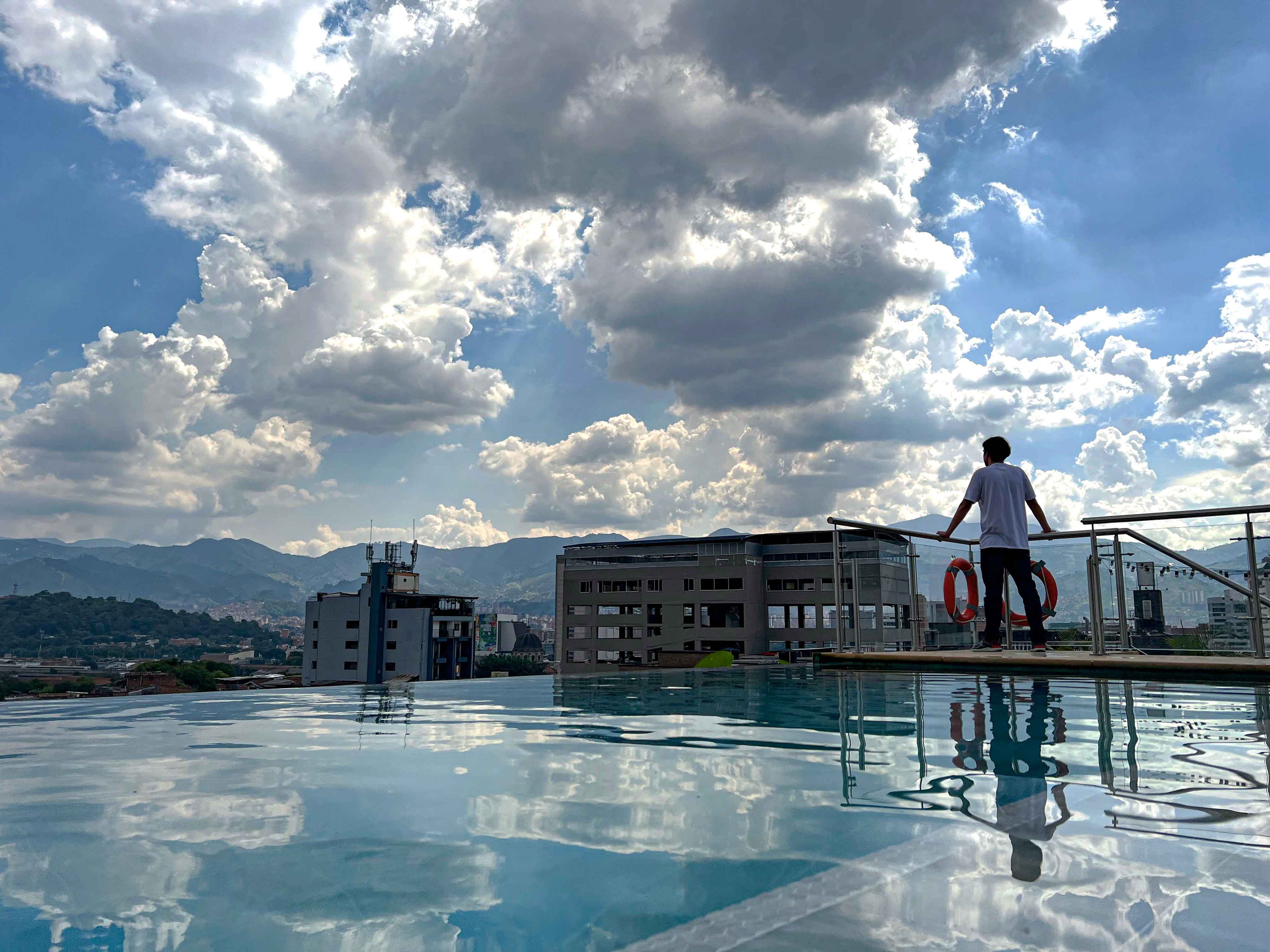 Eine Person steht am Pool, im Hintergrund ein klarer Himmel und Berge.